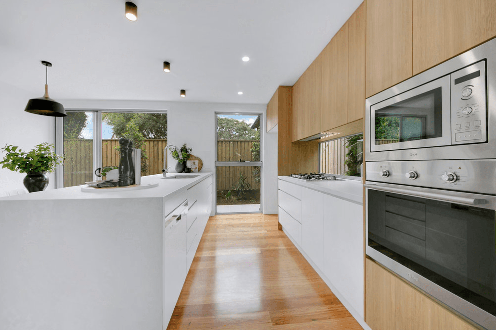 A kitchen with white cabinets , wooden floors , and stainless steel appliances.