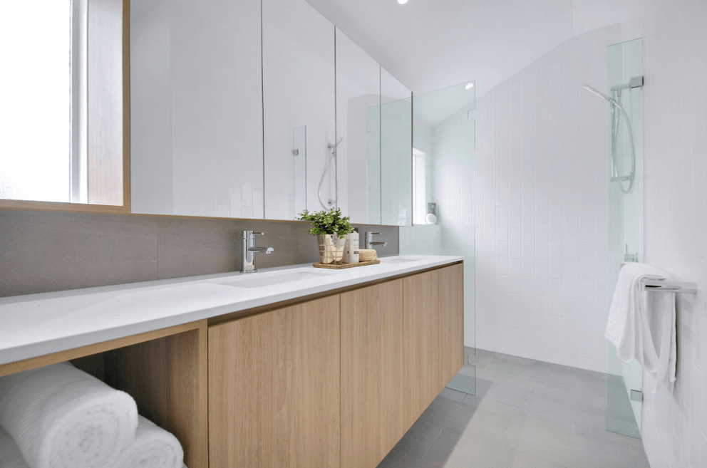 A bathroom with two sinks , a mirror and a walk in shower.