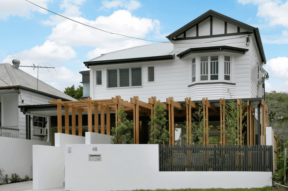 A white house with a wooden pergola on the front of it.