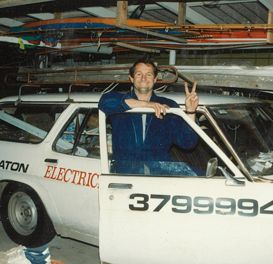 A man giving a peace sign in front of an electric car