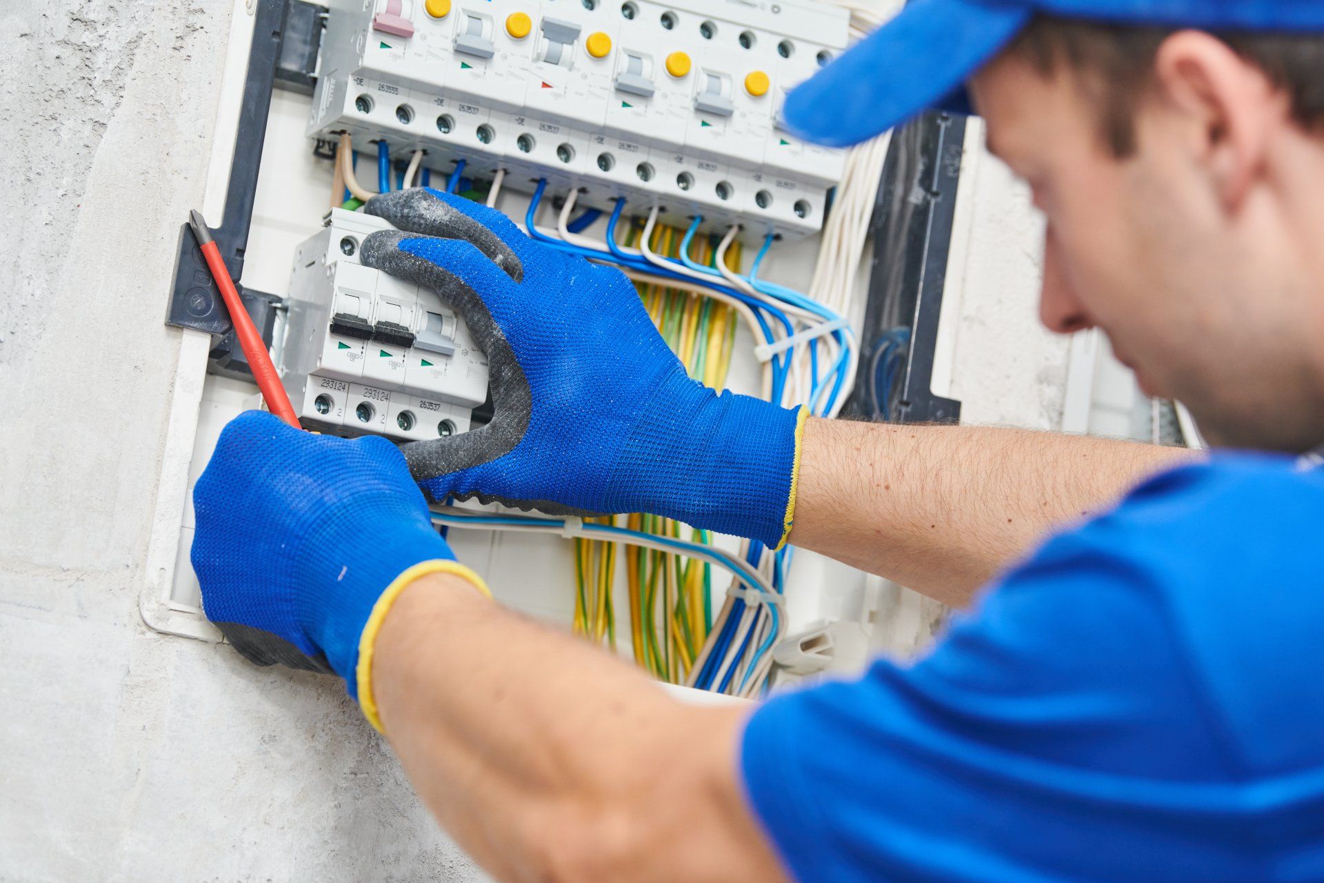 A man in a blue shirt and hat is working on an electrical box.