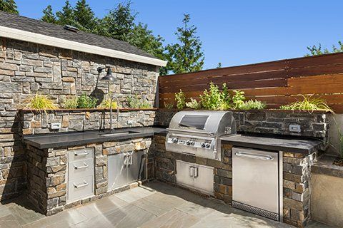 Outdoor kitchen with stone counters and stainless steel appliances; features a grill, sink, and refrigerator.