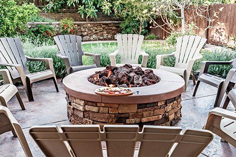 Fire pit surrounded by plastic Adirondack chairs in a backyard setting.