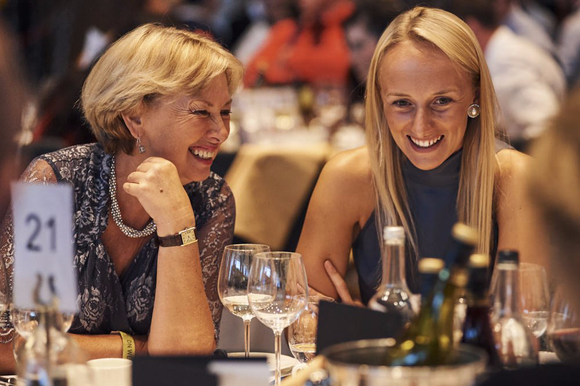 Two women are sitting at a table with wine glasses and smiling.