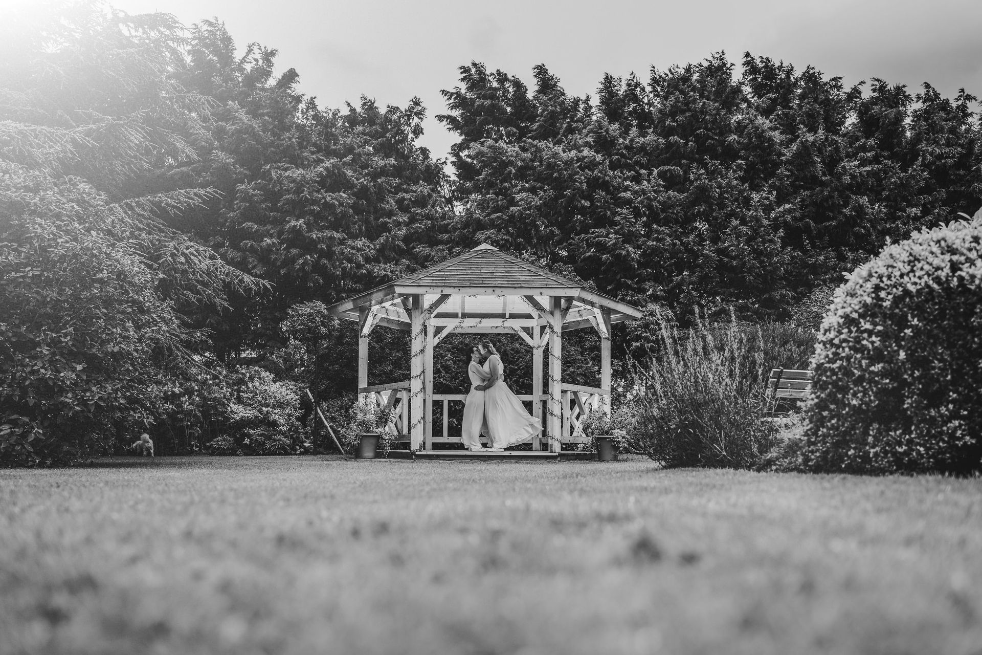 A black and white photo of a bride and groom standing under a gazebo.