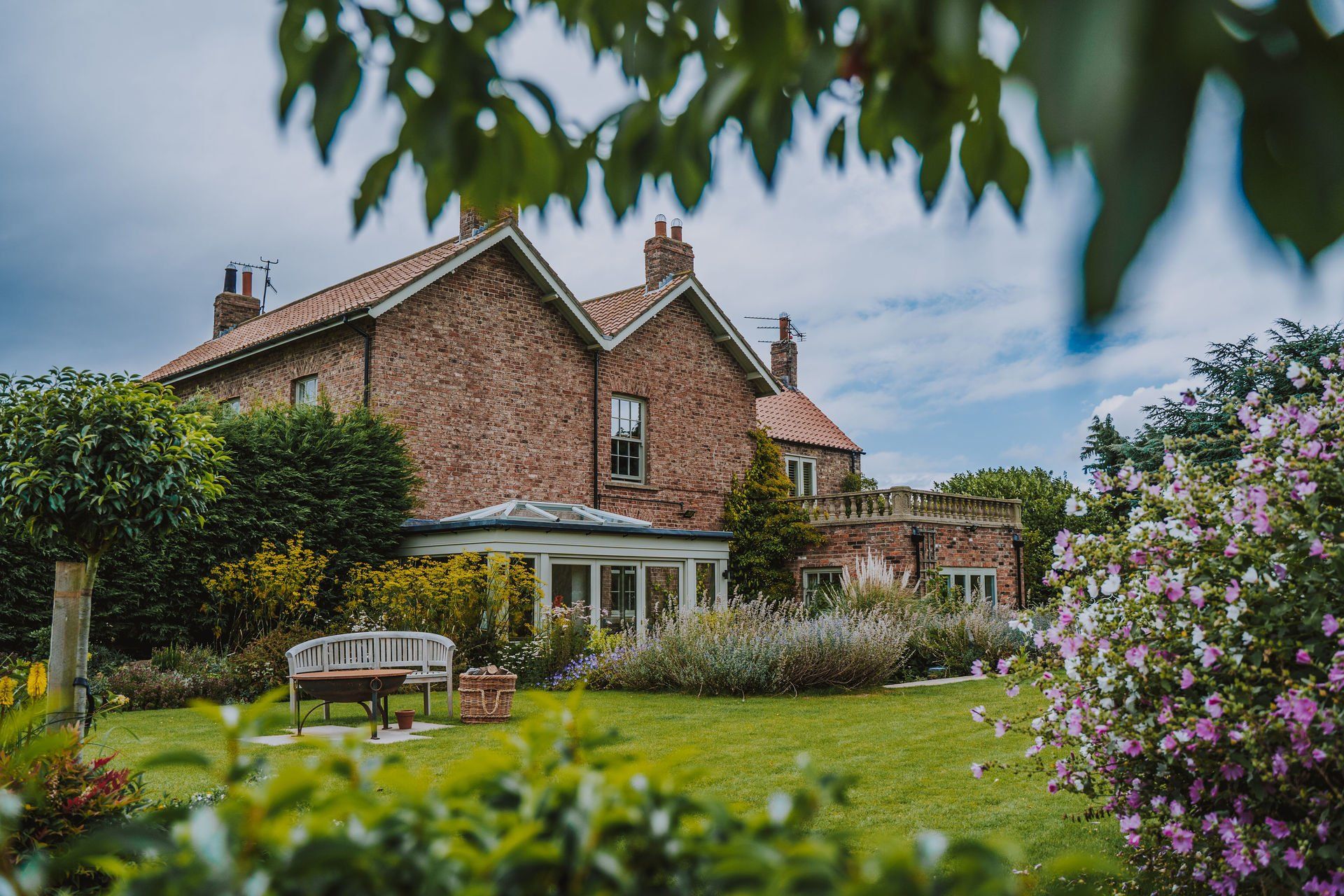 A large brick house with a lush green garden in front of it.