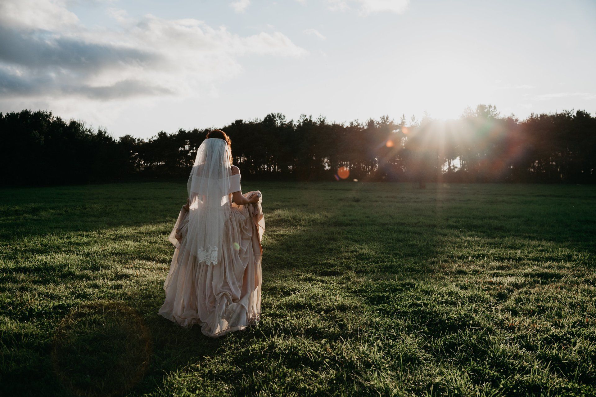 A bride and groom are walking through a grassy field.