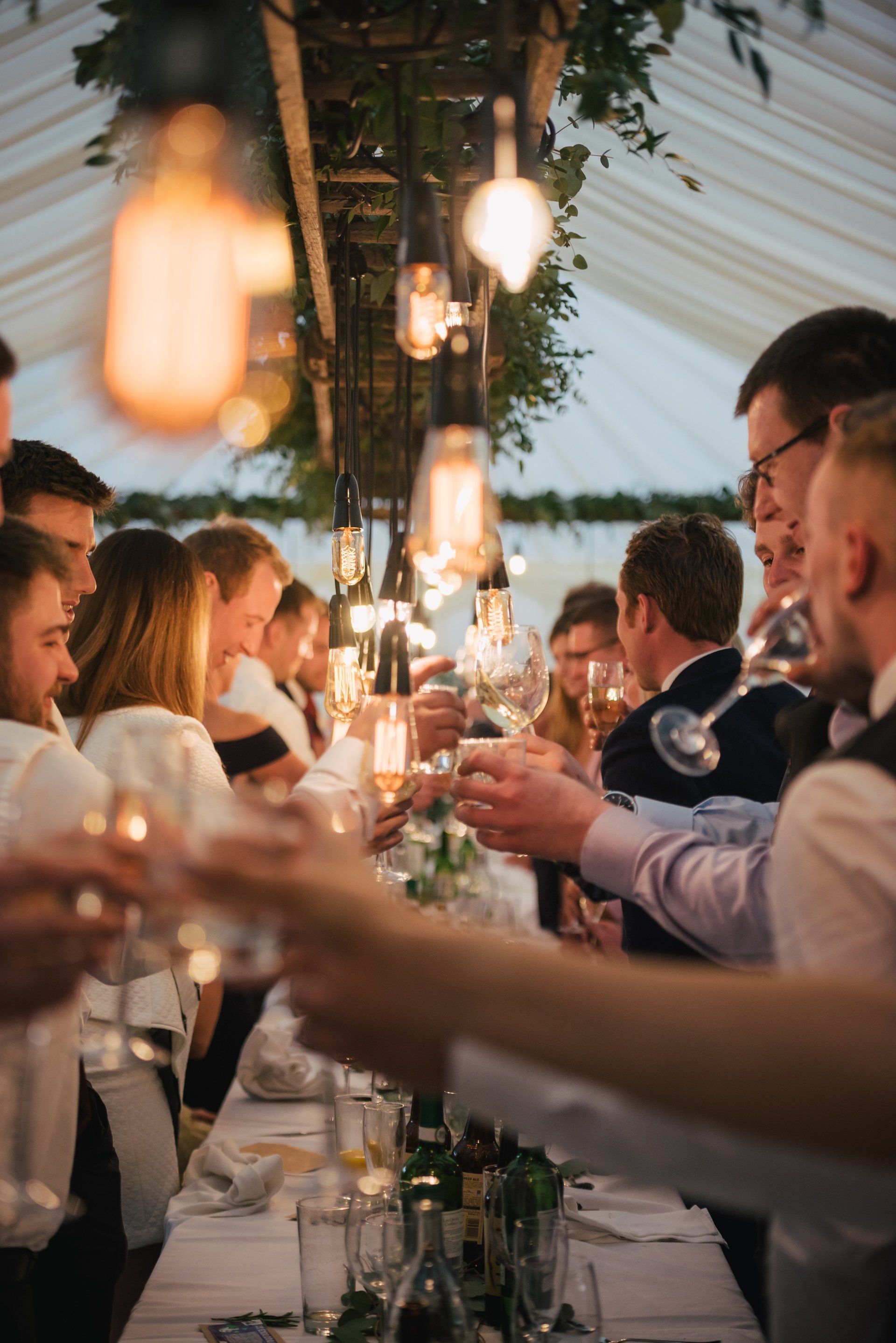 A group of people are sitting at a long table toasting with wine glasses.