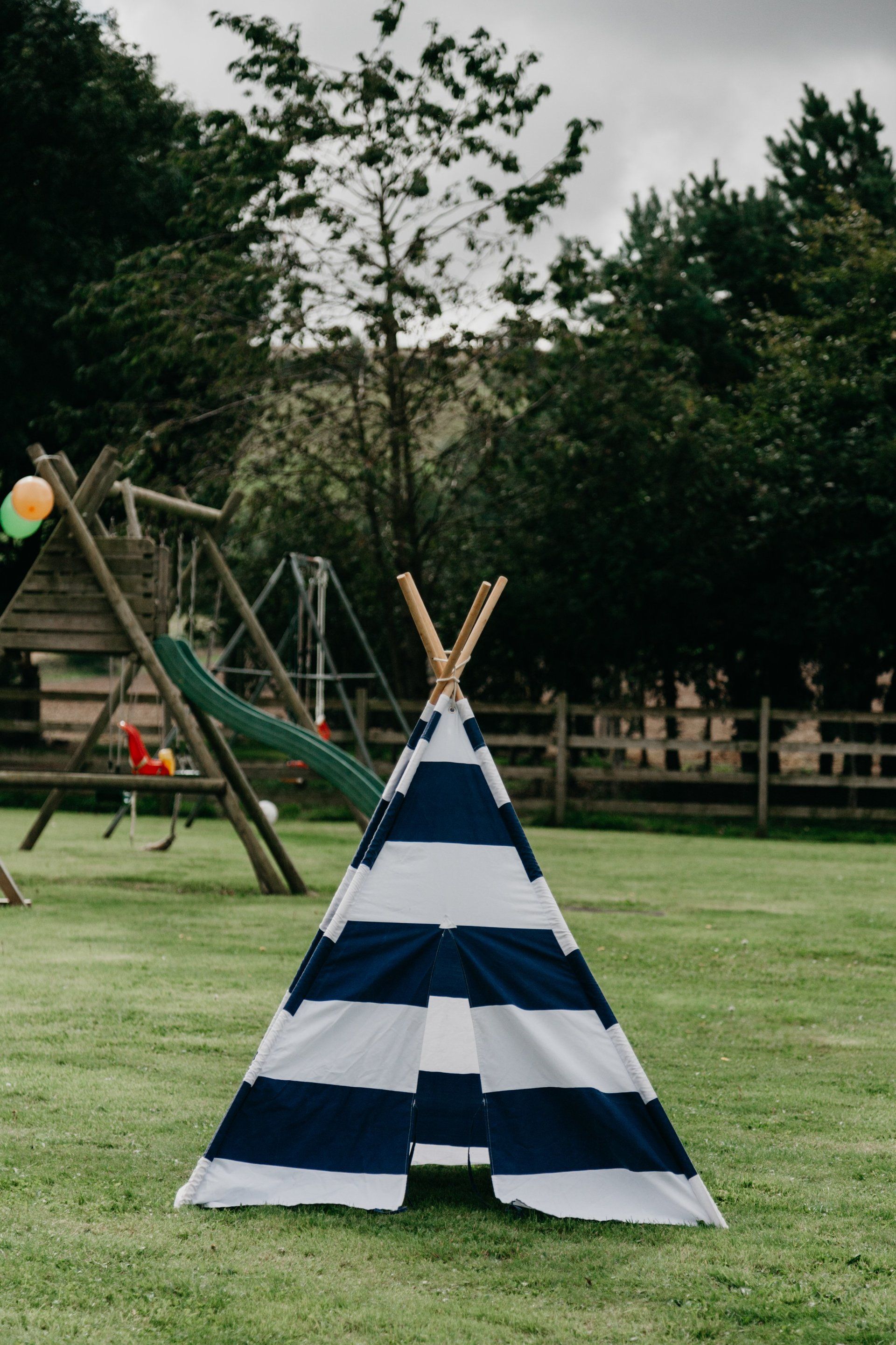 A blue and white striped teepee is sitting in the grass in front of a playground.