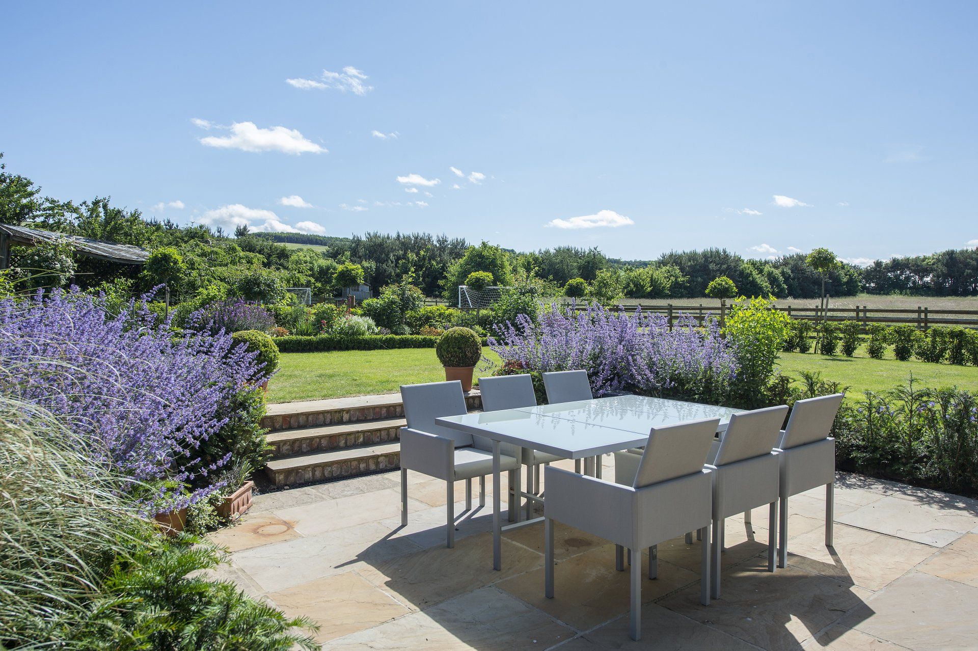 A patio with a table and chairs in the middle of a garden.