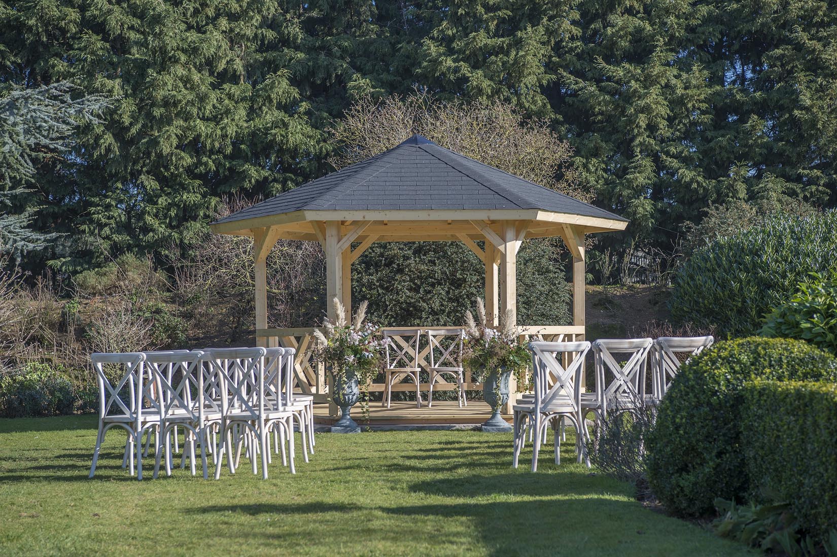 A gazebo with chairs in front of it in a garden.