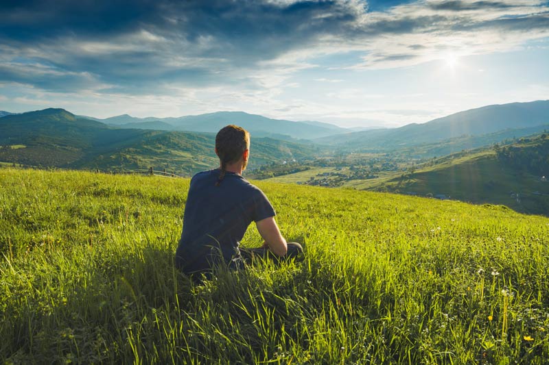 A person sitting on a grassy hill overlooking a valley.