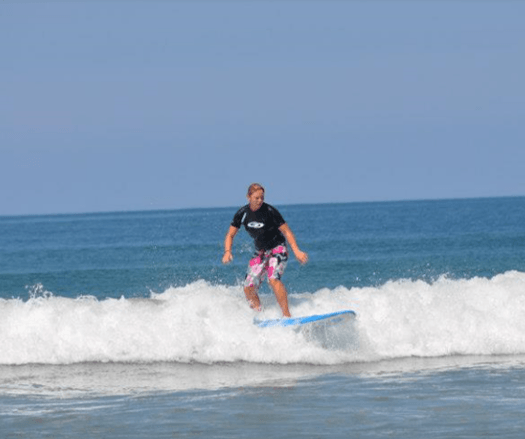 Surfer riding a blue board on a small wave in the ocean under a clear sky