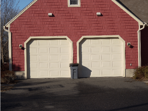 Red garage with two white doors, a trash can, and a dark driveway.