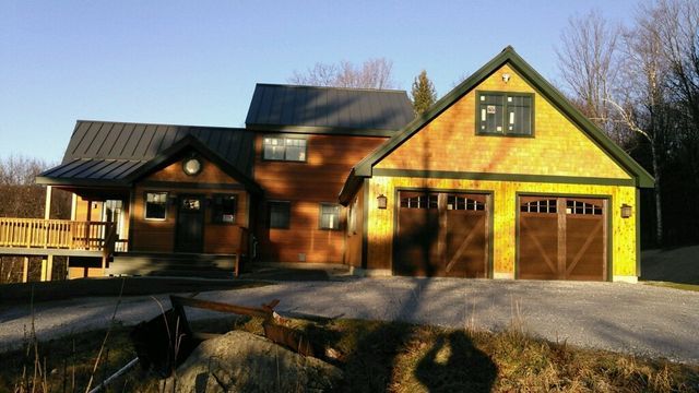 Wooden house with a porch, attached garage with brown doors, and a driveway.