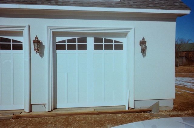 White garage doors with windows, on a white building, brown earth below.
