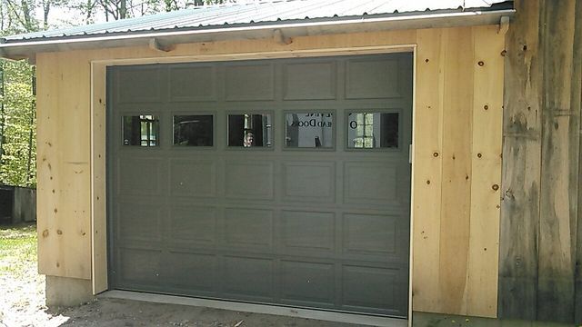 Green garage door with small windows, wooden frame, set in a wood building.