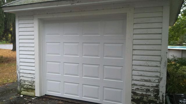 White garage door on a small weathered building with white siding.