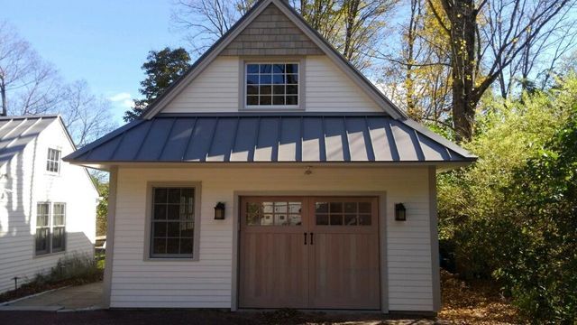 White and tan garage with gray metal roof, wooden door, and small window.