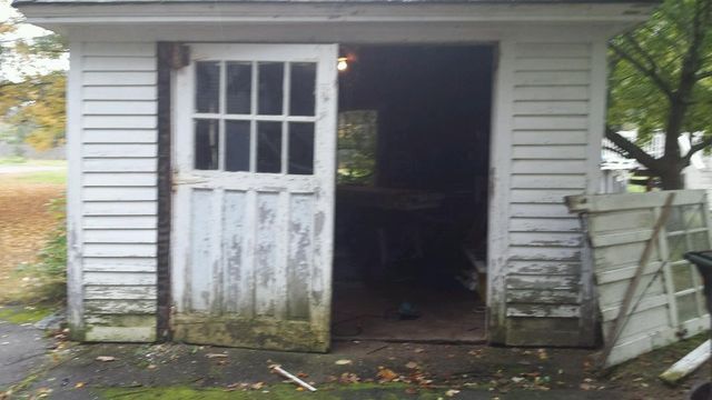 White shed with open door, peeling paint, and clutter inside.