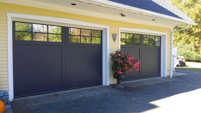 Two charcoal-colored garage doors with windows, set in a yellow house with white trim.