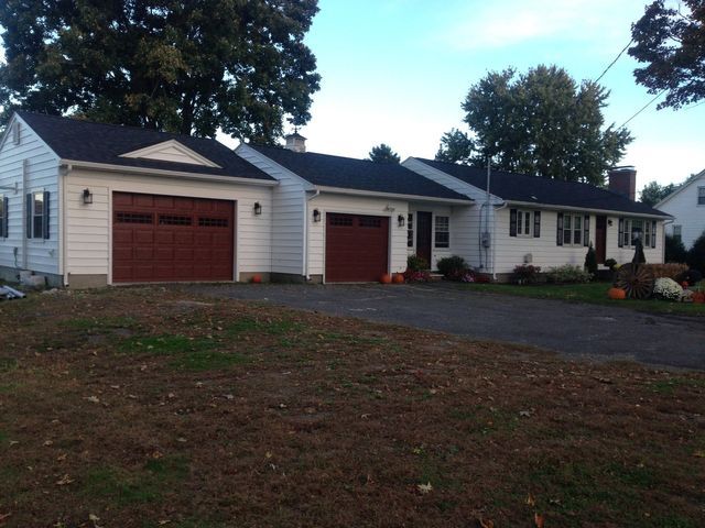 White house with two brown garage doors and a driveway, pumpkins decorate the front yard.