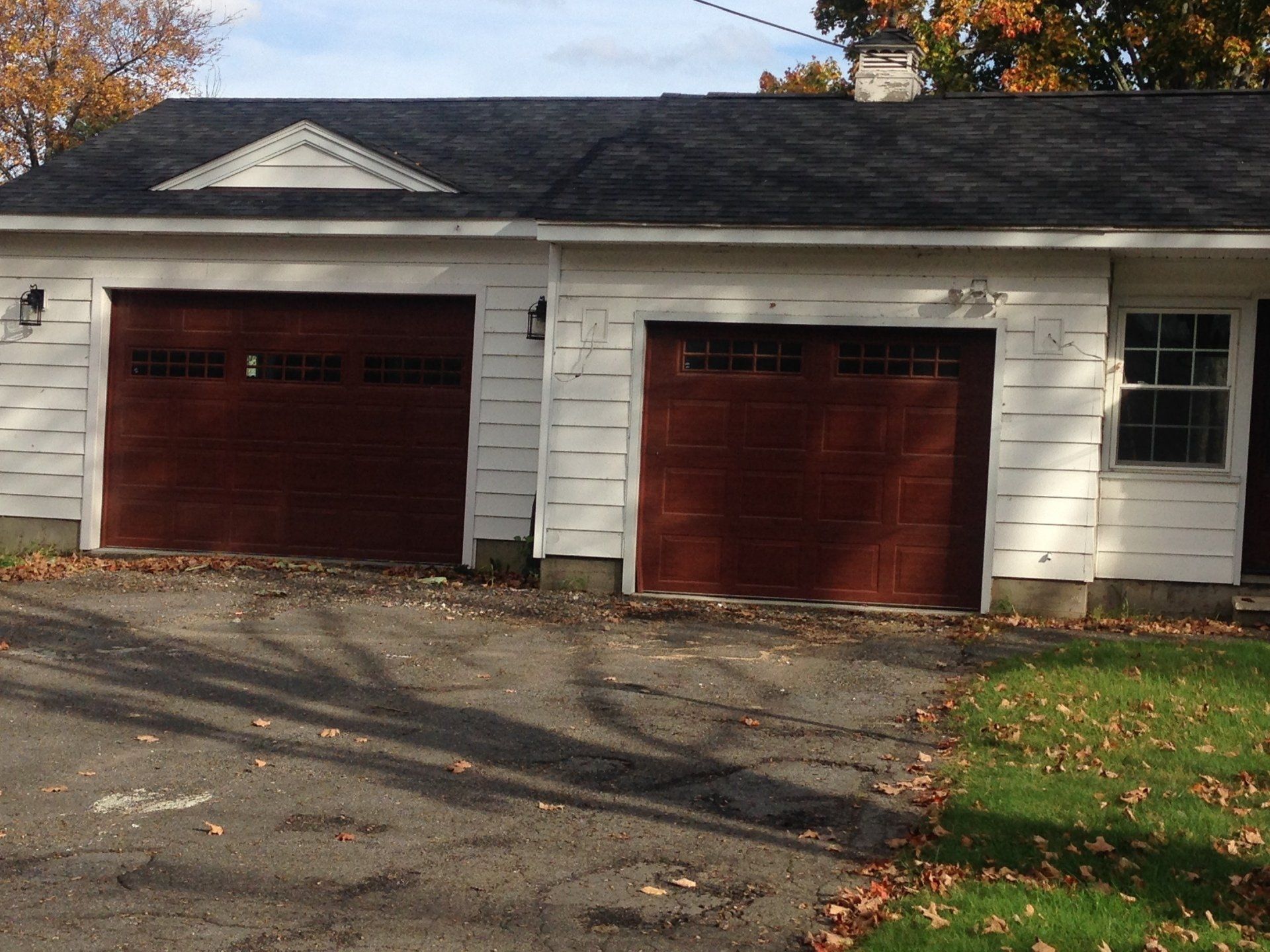 Two-car garage with dark red doors and a white exterior. Asphalt driveway with fallen leaves.