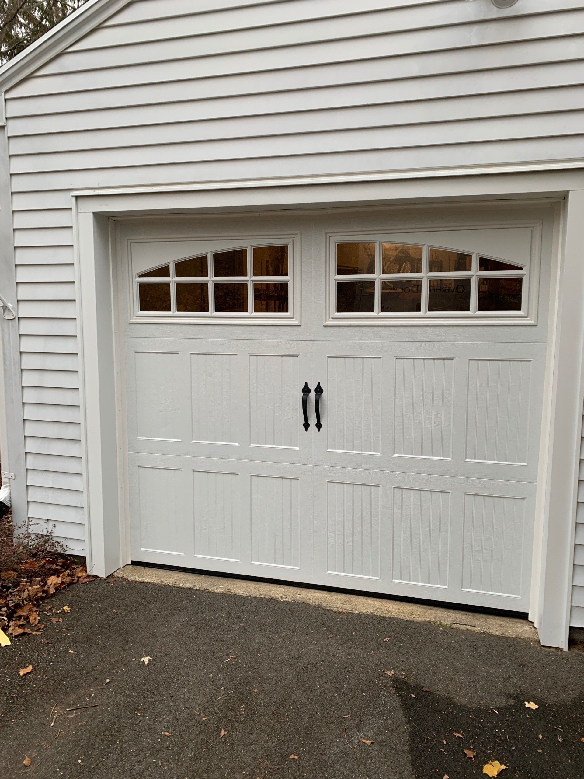 White garage door with arched glass windows, black handles, set in white-sided building.