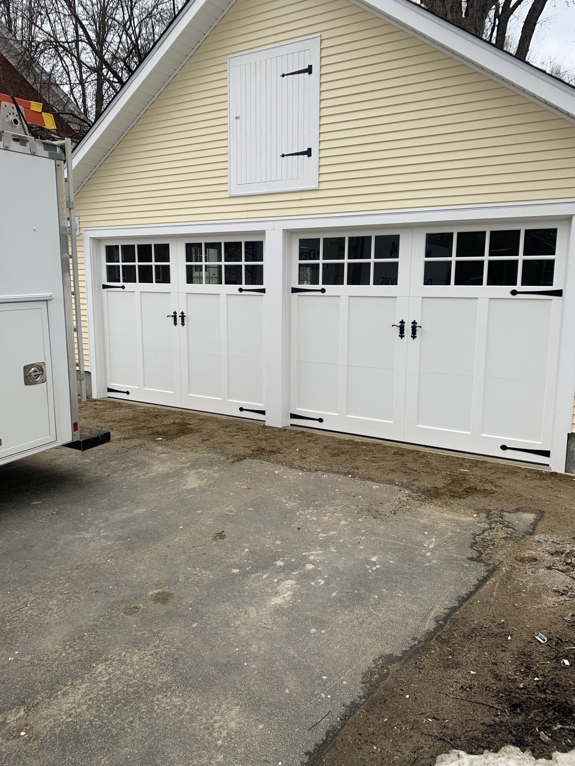 Two white garage doors with black hardware, yellow siding, and an asphalt driveway.