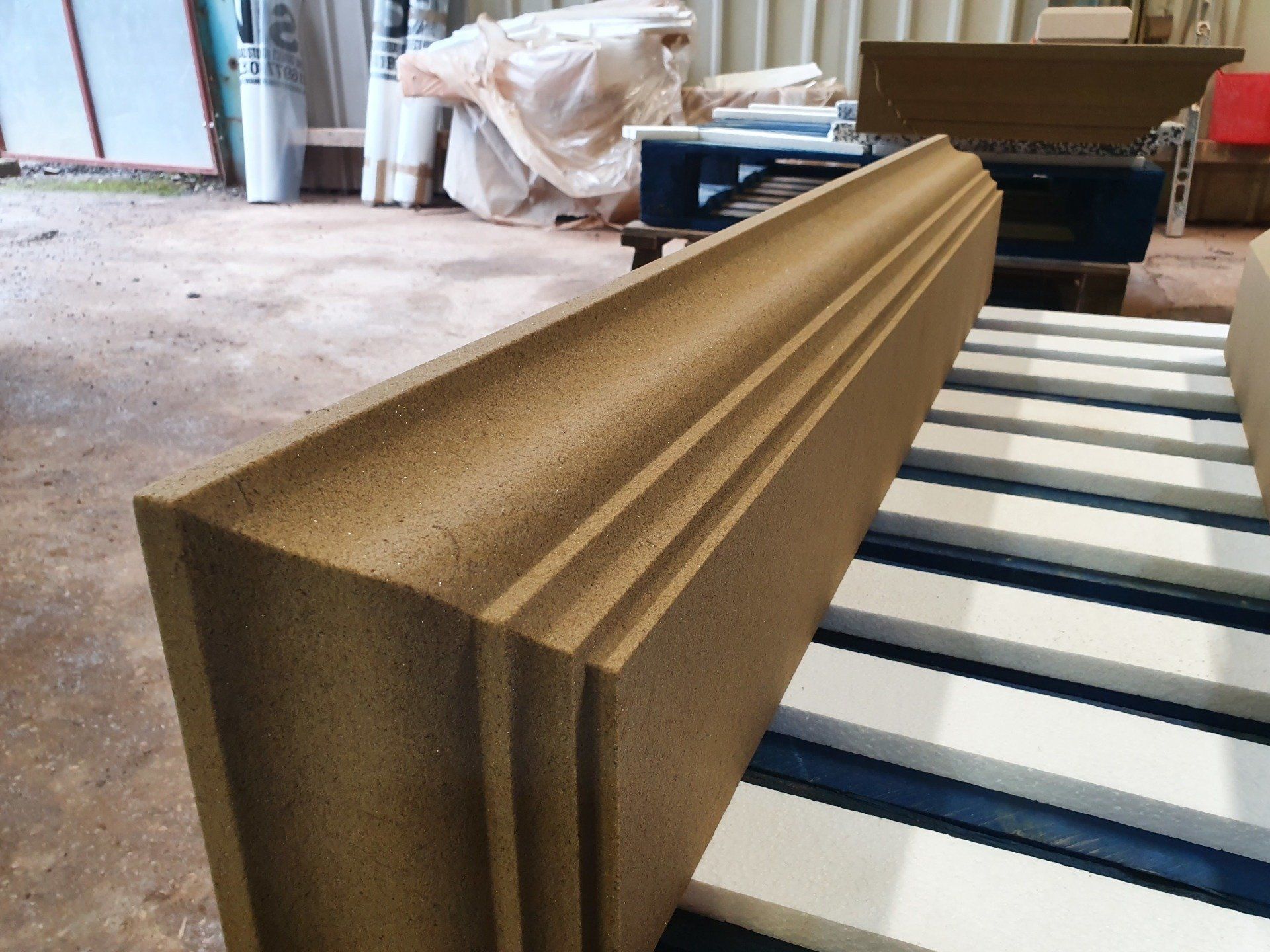 Stacked tan foam panels on a striped pallet in a warehouse.