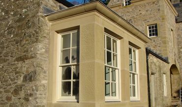 Stone building with cream bay windows and white trim in sunlight