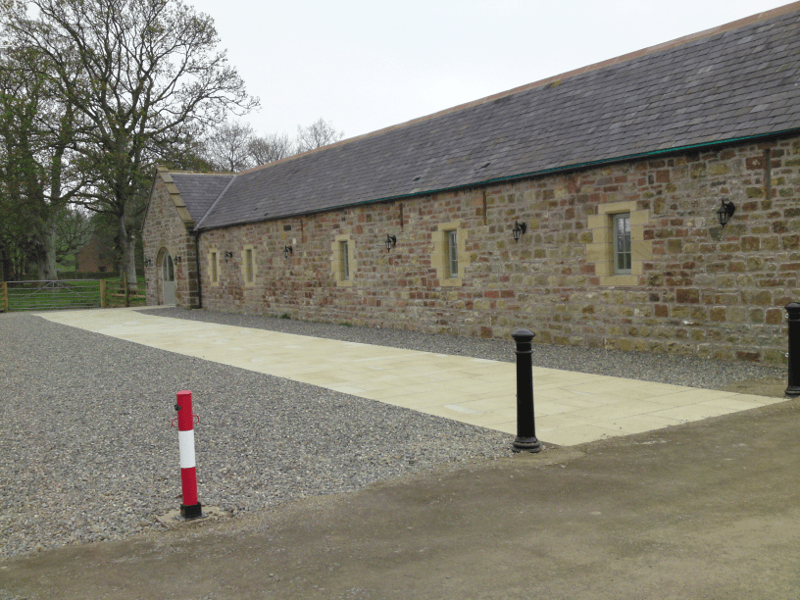 Stone building with small windows beside a gravel path and paved walkway, with trees in the background