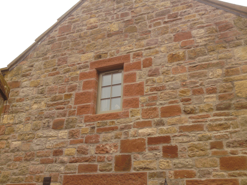 Stone wall of a building with a small window framed in red brick