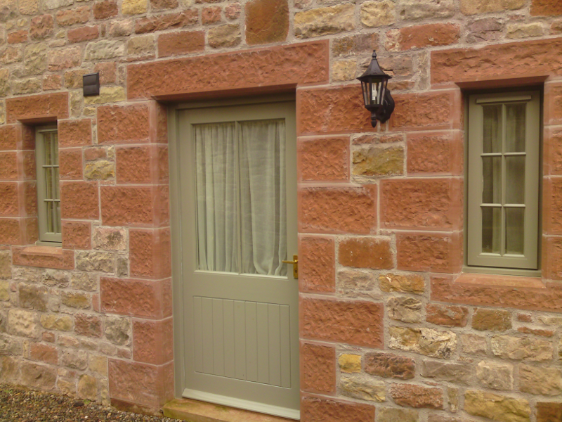 Stone house exterior with a light green door, narrow window, and wall-mounted lantern
