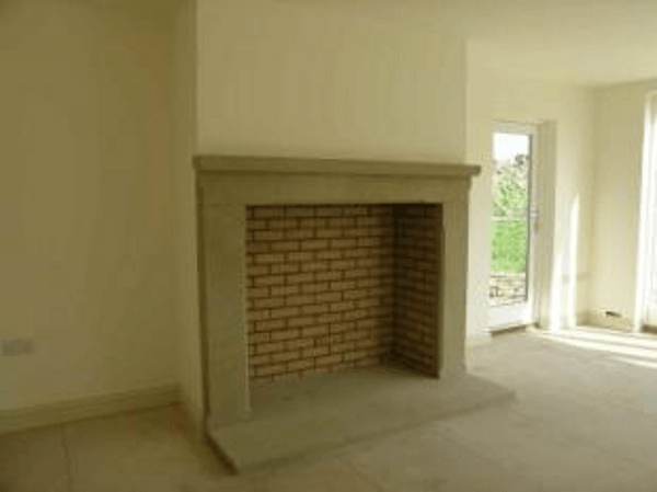 Empty beige room with a brick fireplace and a window letting in daylight