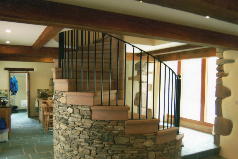 Staircase with stone base, wooden steps, and black railing in a rustic interior room