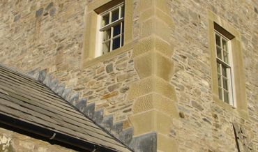 Stone building corner with tan brick trim, tall windows, and a sloped roof