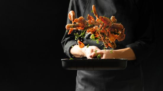 padella con gamberi saltati e cuoco vestito di nero