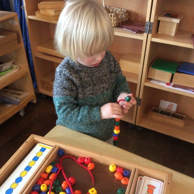 Child threading colorful beads at a wooden table in a playroom