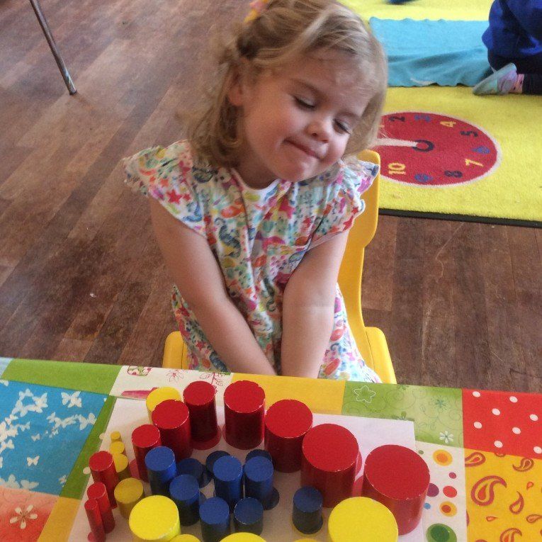 Child sitting at a table playing with colorful stacking blocks in a classroom.