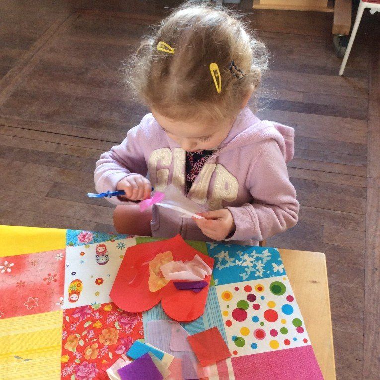Child with hair clips using scissors to cut colorful paper at a craft table.