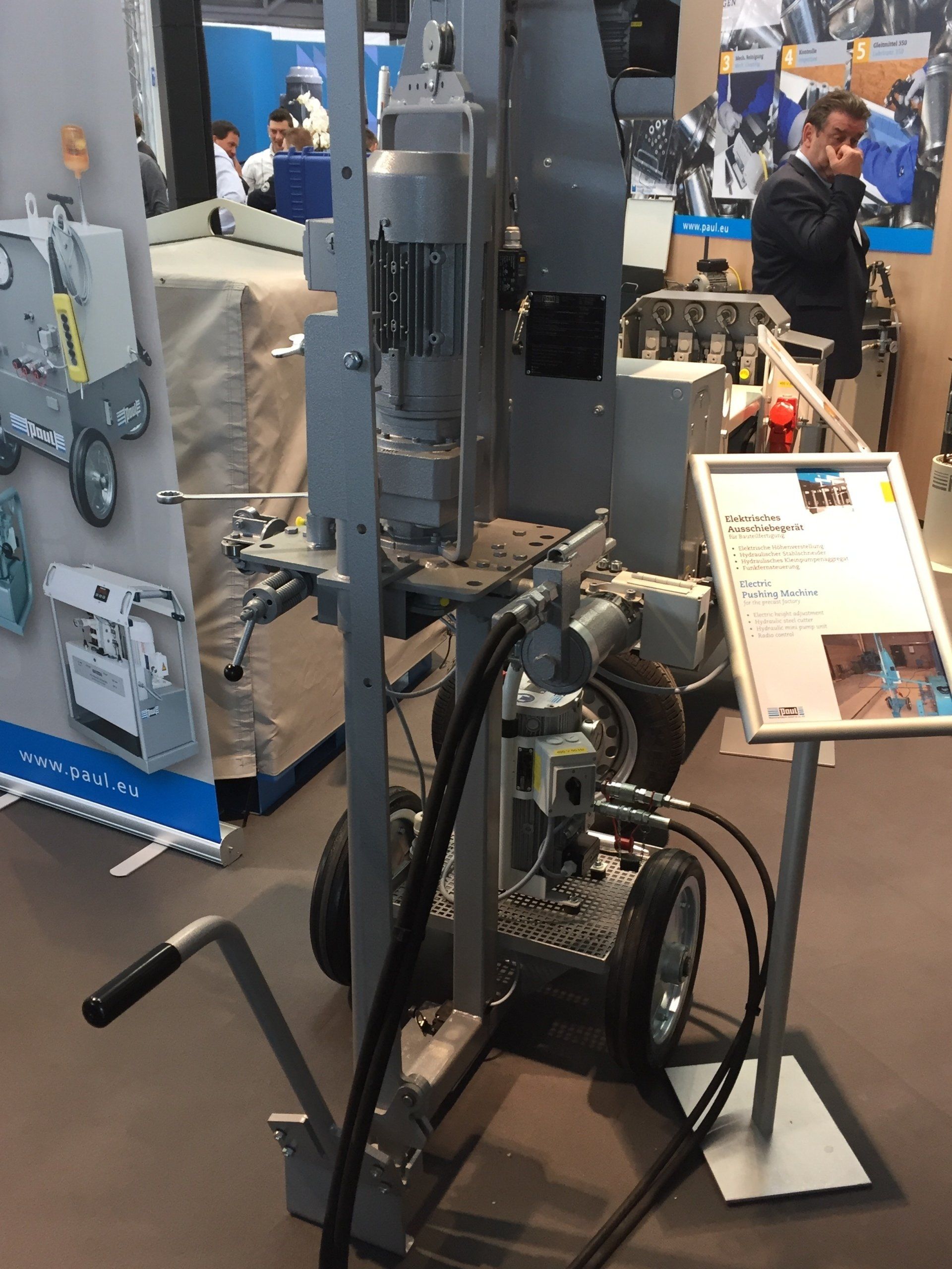 Tall black industrial machine on display at a trade show, with a white information placard nearby.