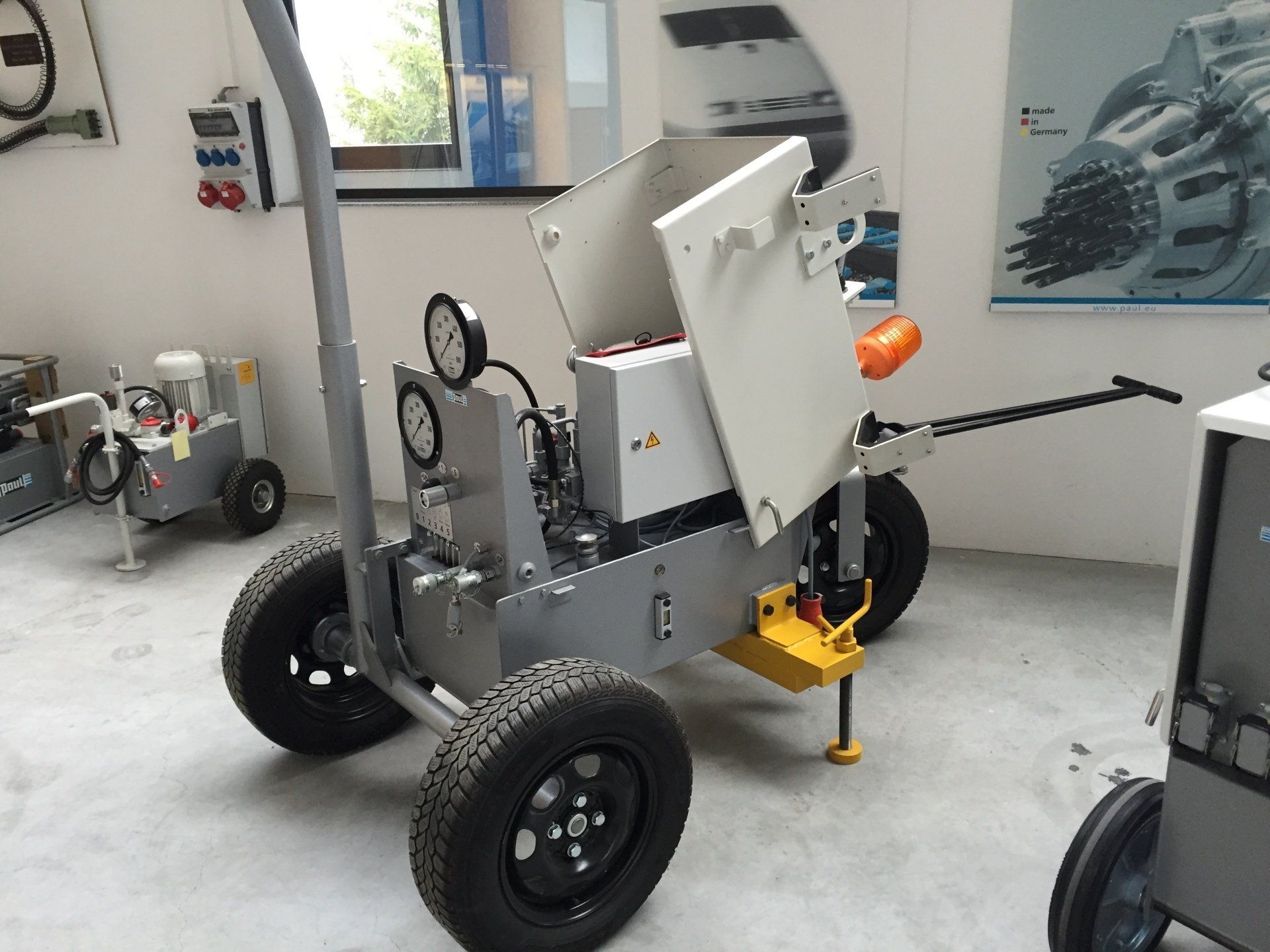Gray robot on wheels in a lab, with a front-mounted arm and orange sensor.