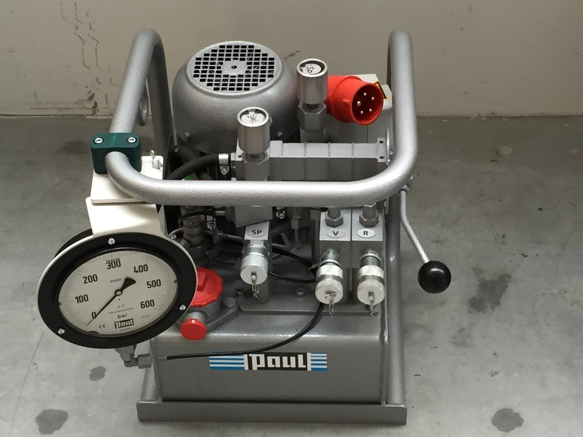 Portable industrial air compressor with gauges, gray frame, and red fittings on a concrete floor