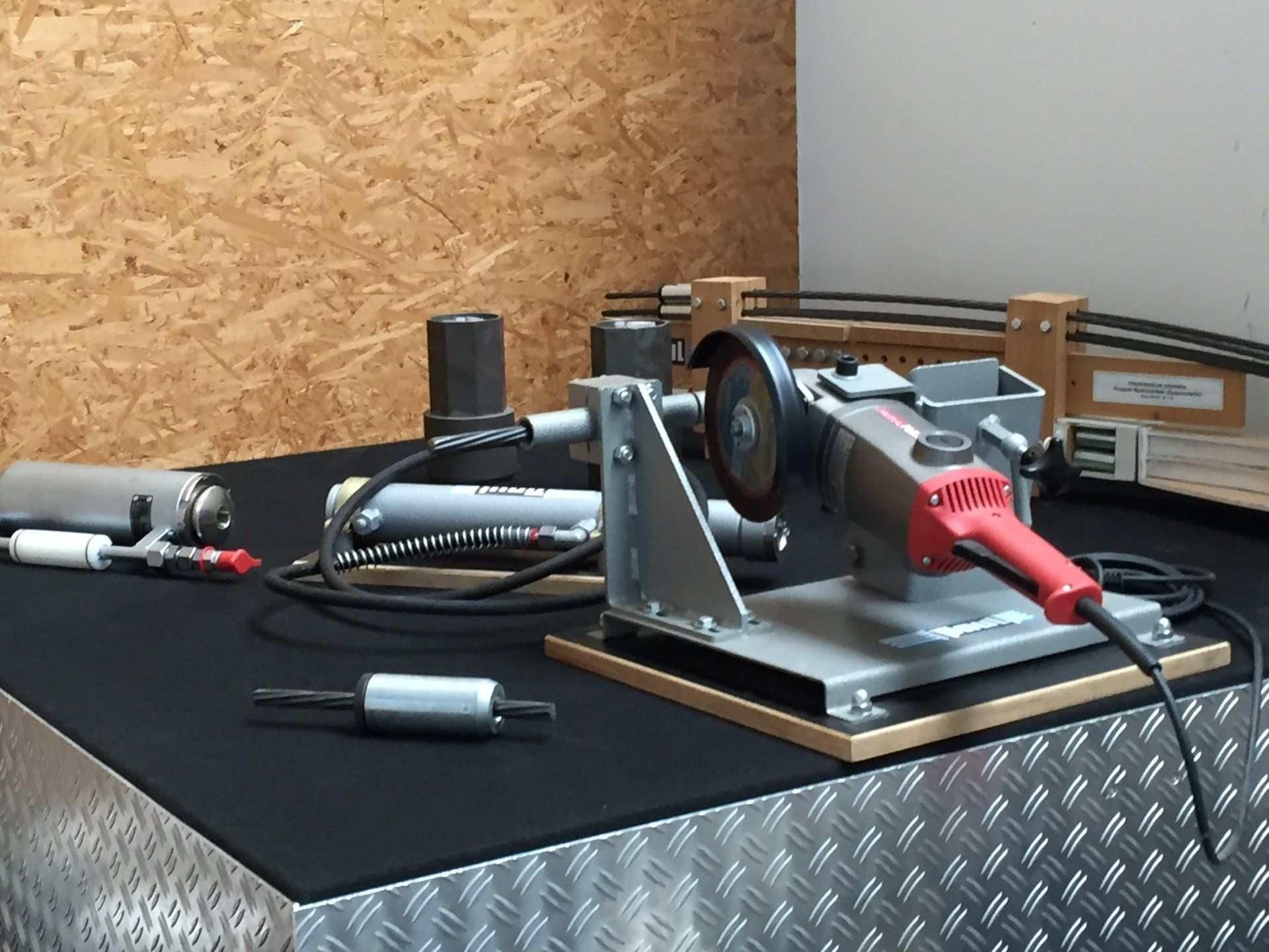 Workbench with a mounted power tool, red drill, and small parts on a black mat in a workshop.