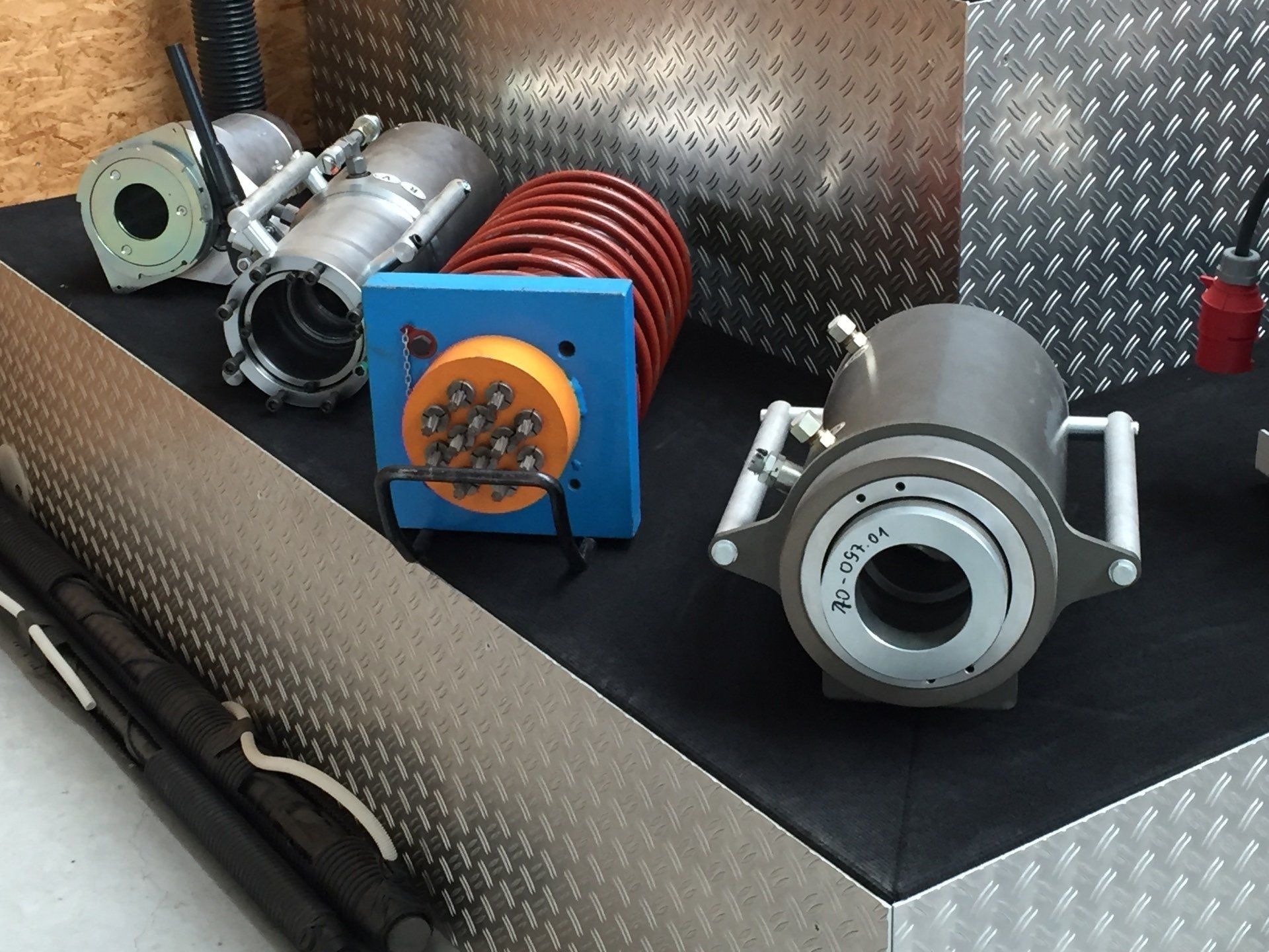 Assorted mechanical components on a black surface, including a red coil, blue box, and silver cylindrical parts.