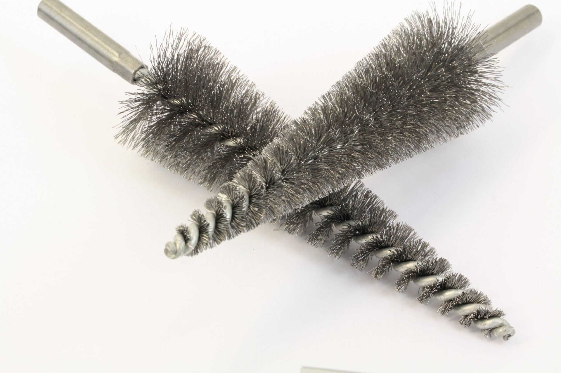 Crossed metal wire tube brushes with wooden handles on a white background
