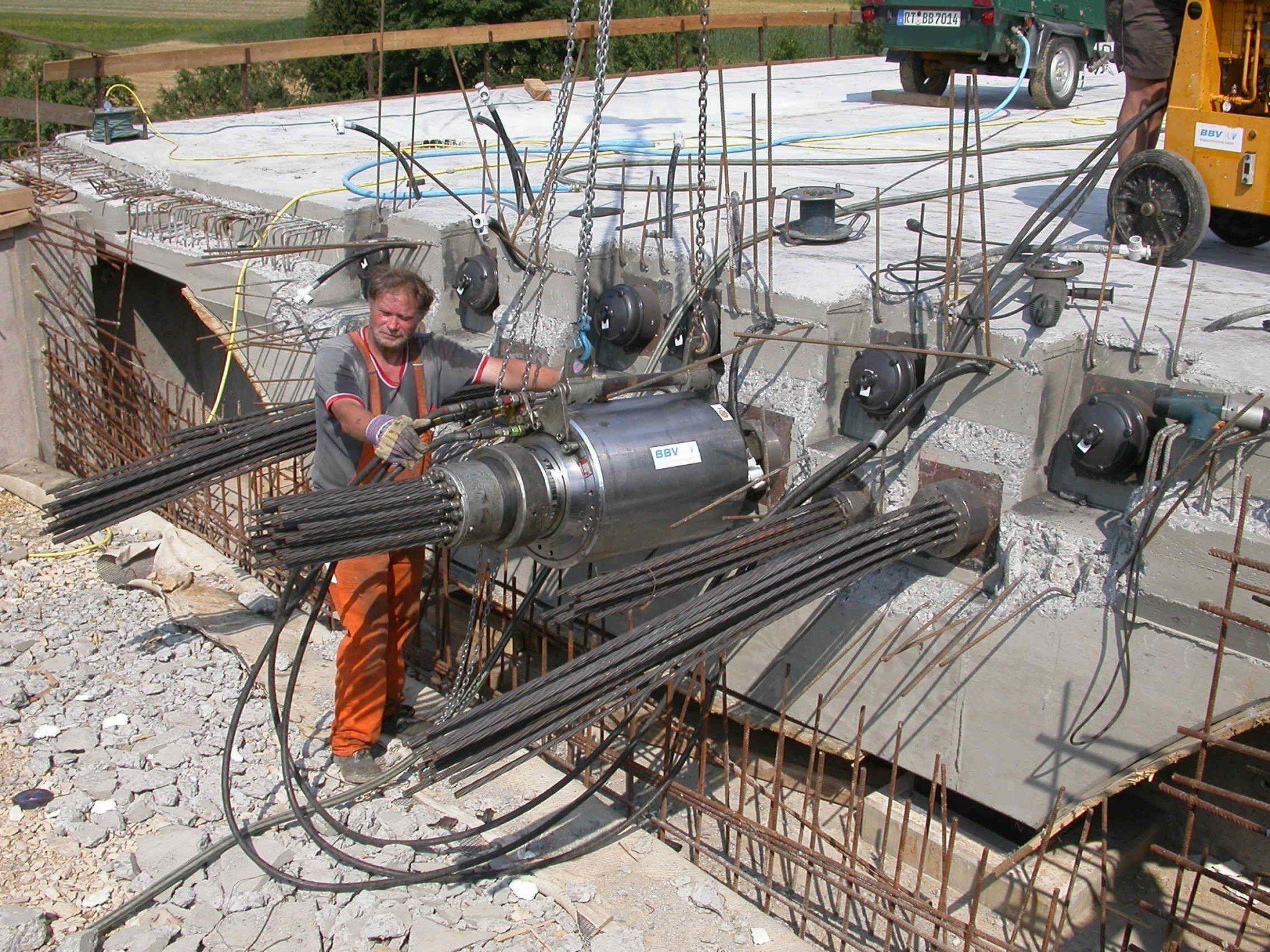 Worker standing by large cylindrical steel structure with exposed rebar and concrete foundation at a construction site