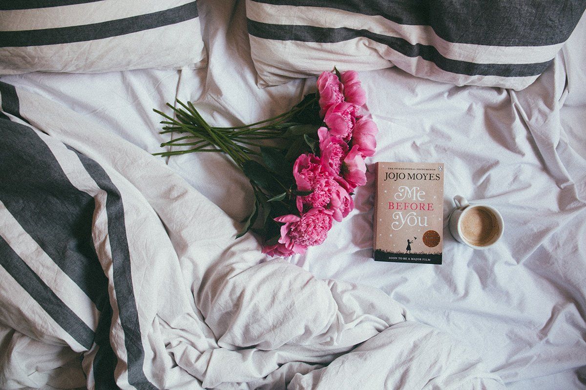 Ein Bett mit einem Buch, Blumen und einer Tasse Kaffee.