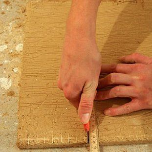 Eine Person misst ein Stück Holz mit einem Maßband.